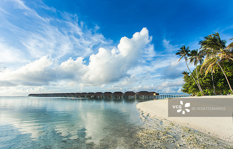 马尔代夫热带岛屿上的水上别墅（小屋），热带海滩上的白色沙滩和蓝色海水图片素材