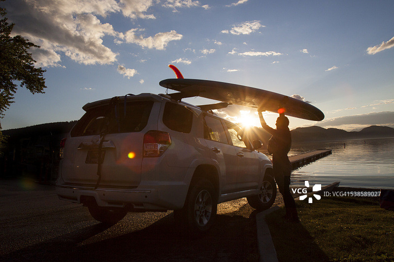 在蒙大拿州白鱼湖日落时将立式桨板放在车上的健壮女人图片素材