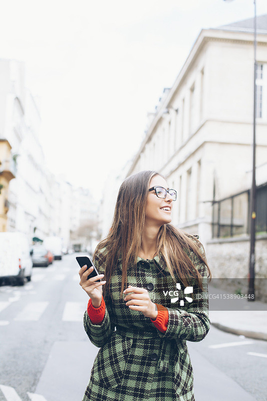 快乐的年轻女子走在街上，手里拿着手机图片素材