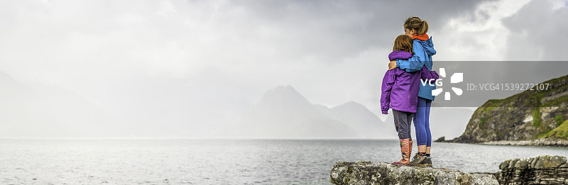 在多岩石的海岸边眺望山海全景的孩子们图片素材