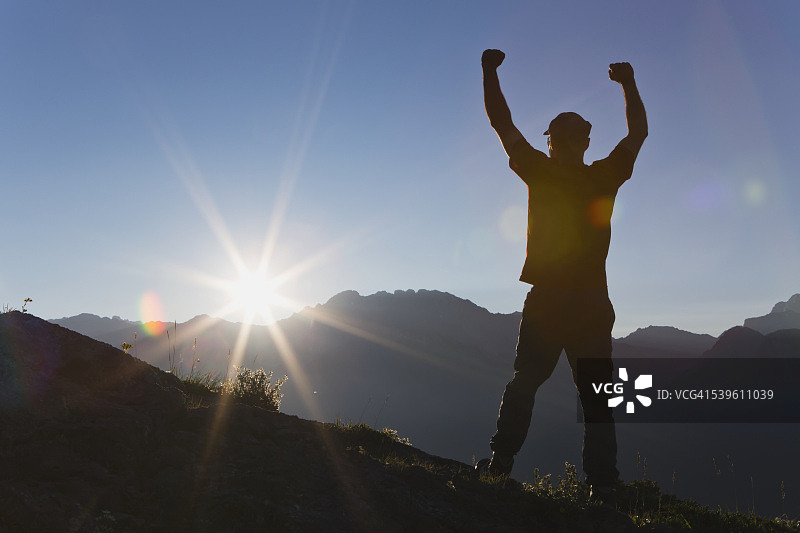 徒步者站在山脊上的轮廓，日出时阳光穿过山脉，蓝天图片素材