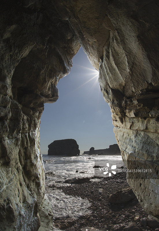 透过天然岩石拱门看岩层和海岸线图片素材