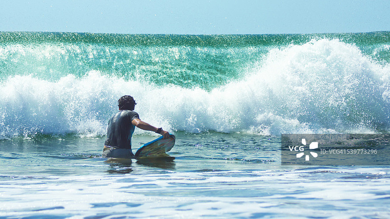 站在海滩巨浪前拿着趴板的男人图片素材