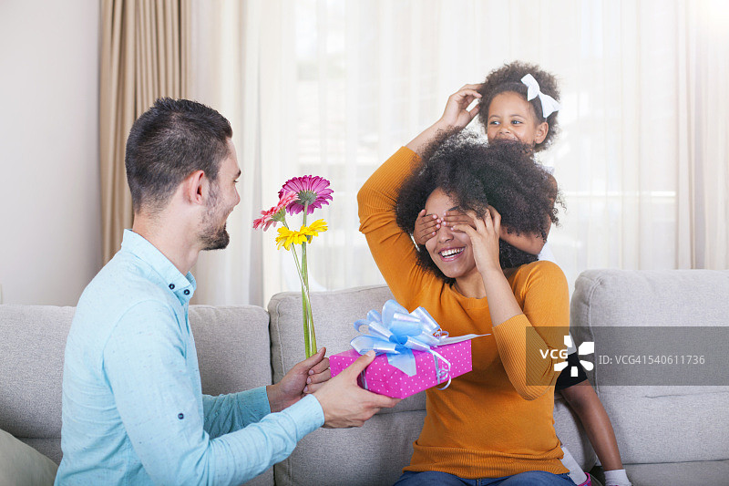 父亲拿着礼物和鲜花，女儿捂住母亲的眼睛图片素材