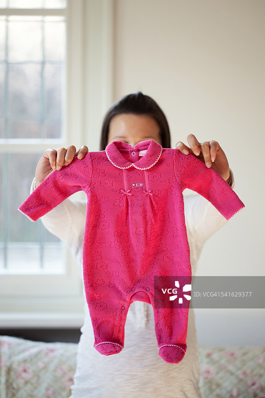 准妈妈在脸前拿着粉红色的婴儿连体衣图片素材