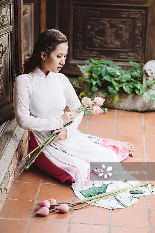 身穿奥黛、手持莲花的越南年轻女性，在怀旧场景中图片素材