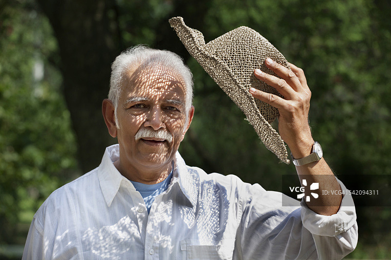 在公园里拿着帽子微笑的年长男人图片素材