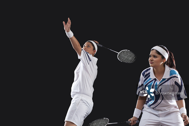 年轻女子在黑色背景上打羽毛球双打图片素材