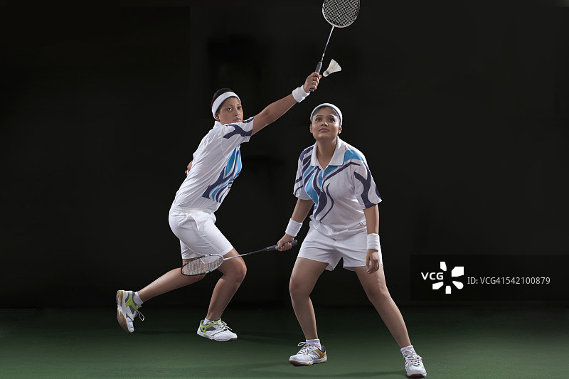 在黑色背景下打羽毛球双打的年轻女运动员图片素材