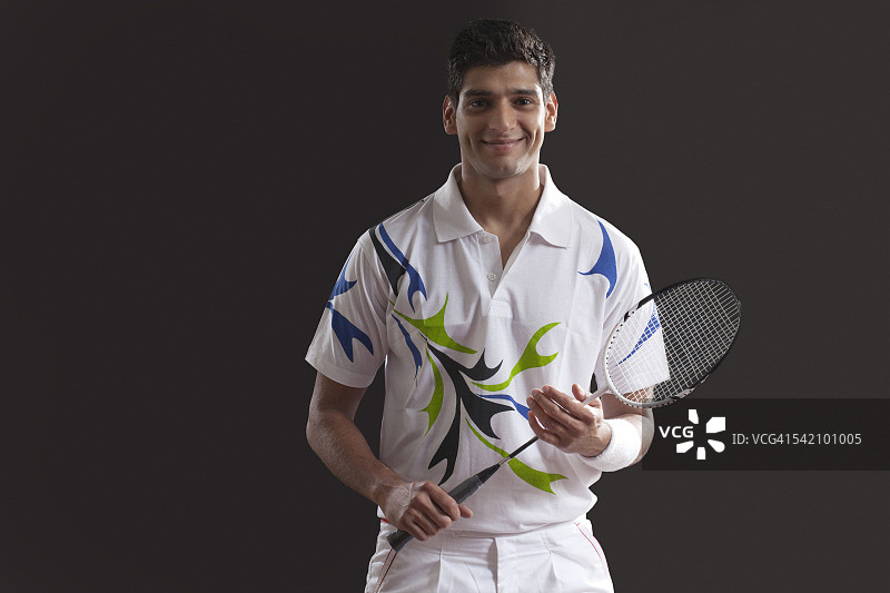 自信的年轻男子拿着网球拍站在黑色背景前的肖像图片素材