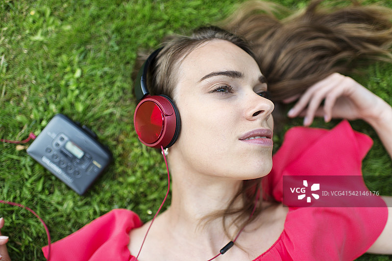 年轻女人躺在公园的草坪上，用随身听听音乐图片素材