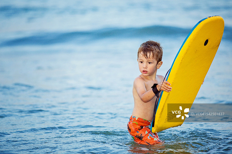 男孩拿着冲浪板站在海里图片素材