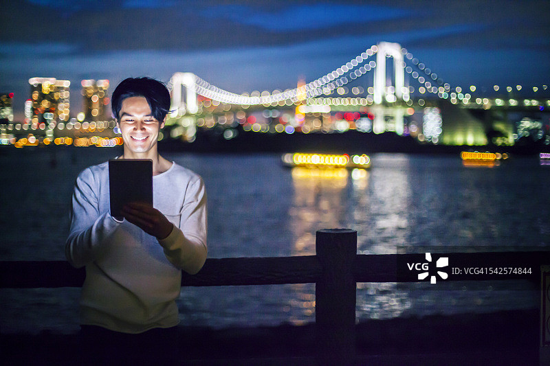 站在桥上晚上使用平板电脑的男人图片素材