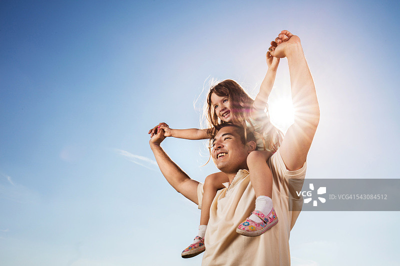 蓝天下，亚洲父亲扛着女儿。图片素材