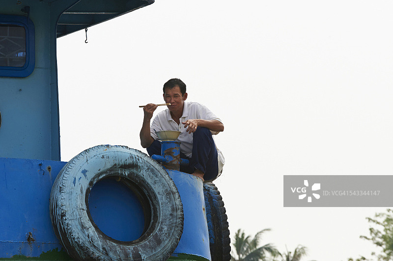 在越南美托湄公河上，男人在船上吃米饭图片素材