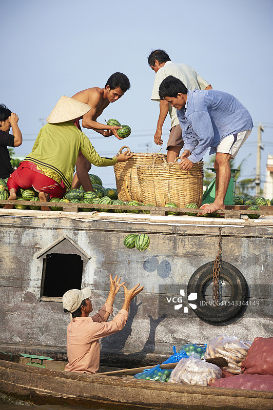 在越南美托，男士们在湄公河上将西瓜扔进市场船图片素材