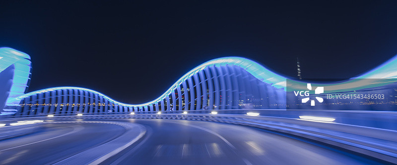 汽车行驶在灯光照亮的蓝色桥梁上的第一人称视角图片素材