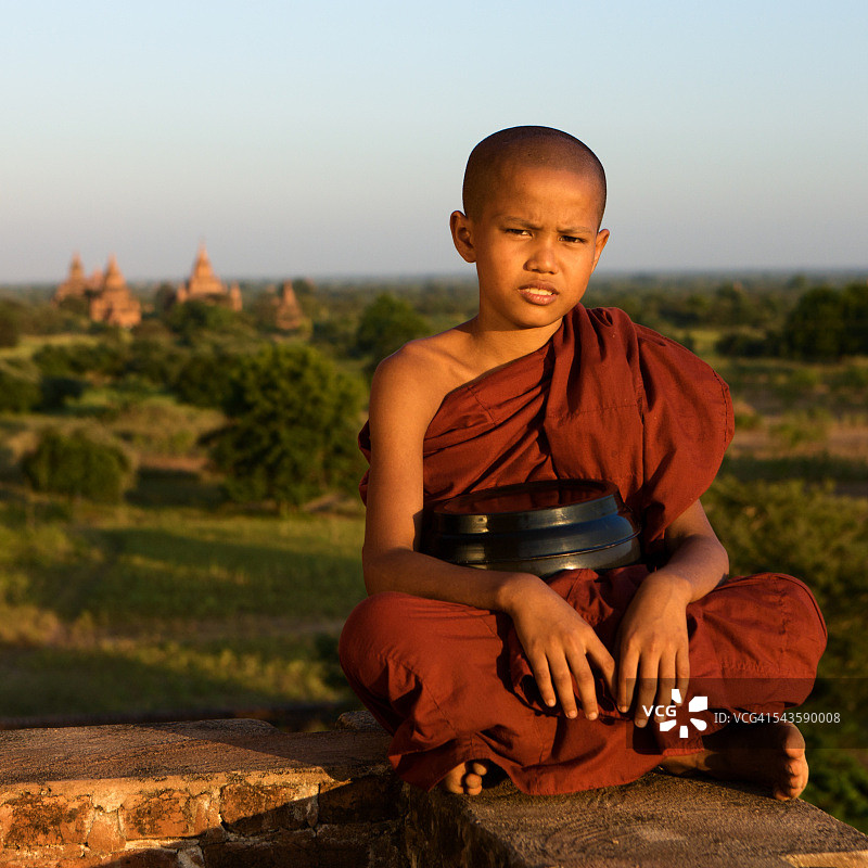 坐在蒲甘寺庙屋顶上的年轻佛教僧侣图片素材