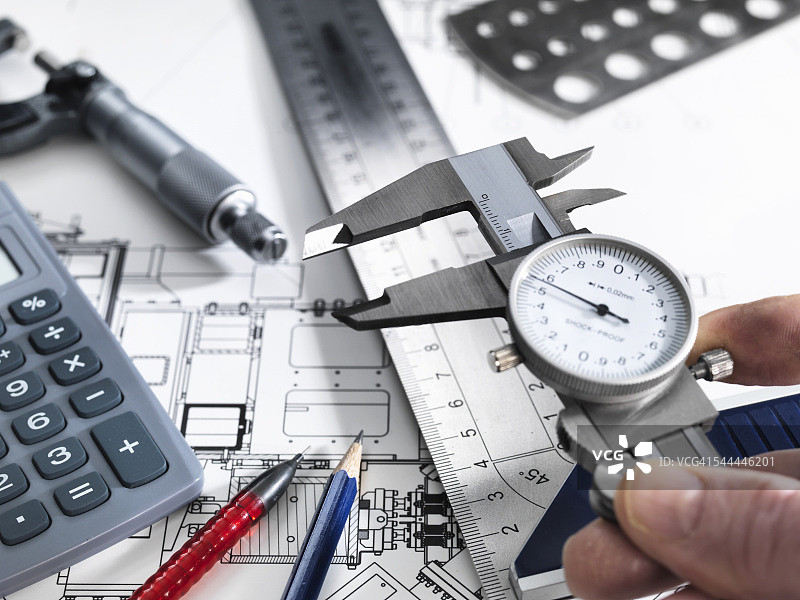工程师手持带测量设备的卡尺，坐在技术图纸旁图片素材