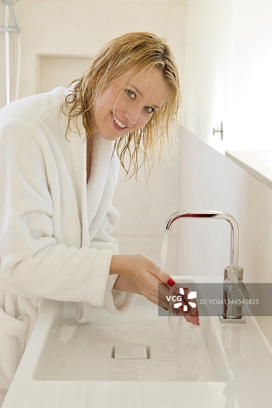 金发年轻女人穿着浴袍洗手图片素材