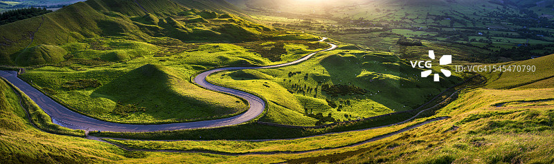 夏季阳光下蜿蜒穿过绿色山丘的乡村道路图片素材