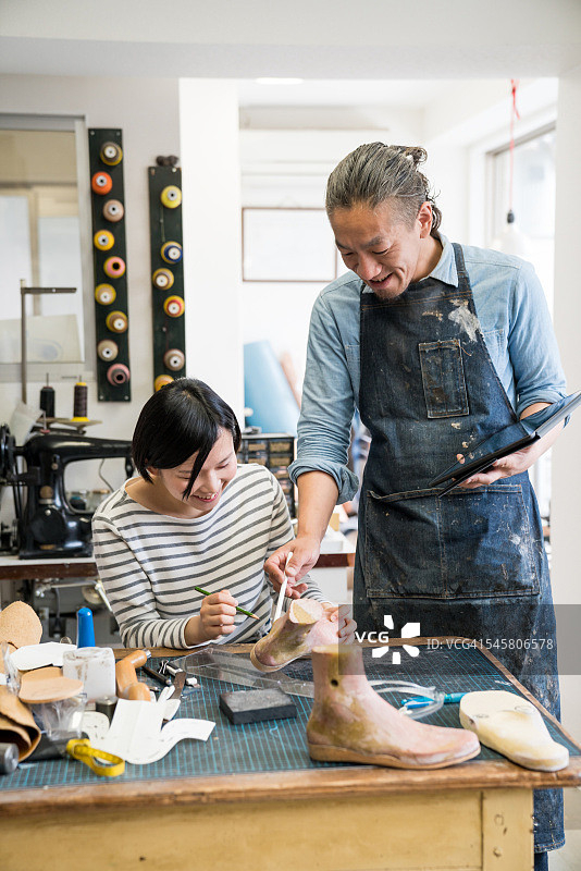 两位鞋匠在鞋店里用数位板讨论图片素材