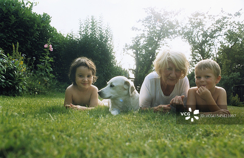 奶奶和孙子们与狗躺在花园的草地上图片素材