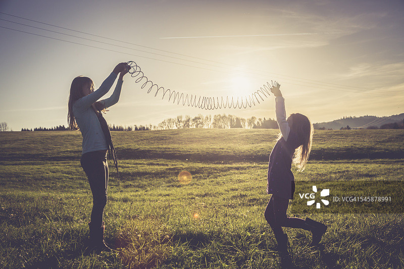 在逆光草地上玩螺旋玩具的两个小女孩图片素材