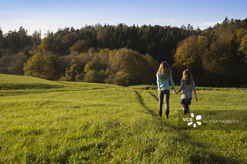 德国巴伐利亚州兰茨胡特：两名女孩在秋季草地上散步图片素材