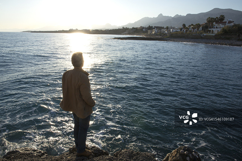 男人从岸边眺望大海和远处的村庄图片素材