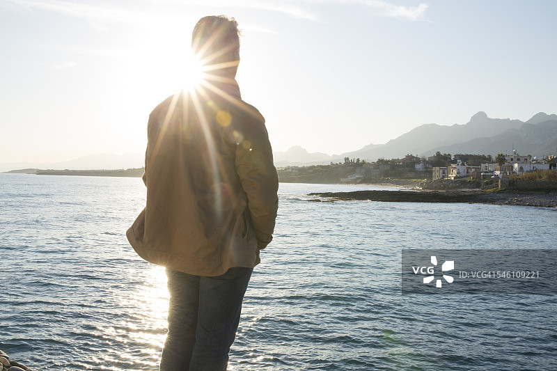 日出时分，男人眺望大海和远处的村庄图片素材