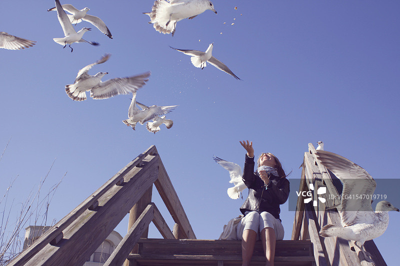 中年妇女在美国佛罗里达州杰克逊维尔海滩喂海鸥图片素材
