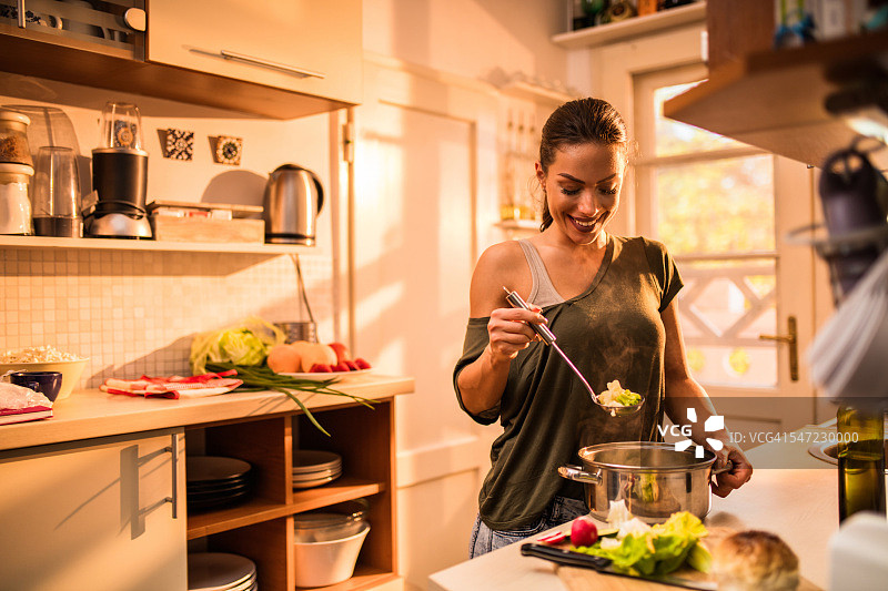 在厨房烹饪蔬菜的年轻微笑女人图片素材