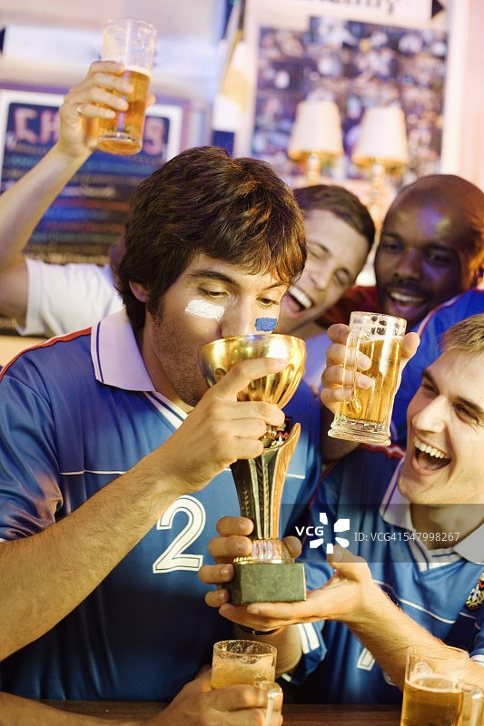足球迷在朋友的帮助下，用奖杯喝水图片素材