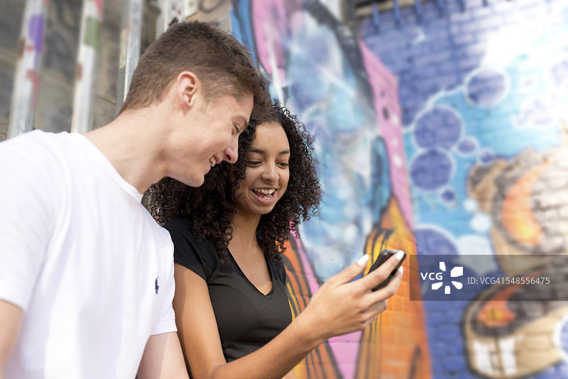 青少年情侣在涂鸦墙边使用智能手机图片素材