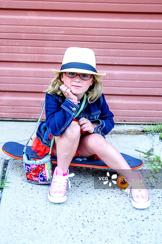 穿着牛仔外套、戴着帽子的芭蕾舞裙女孩坐在滑板上图片素材