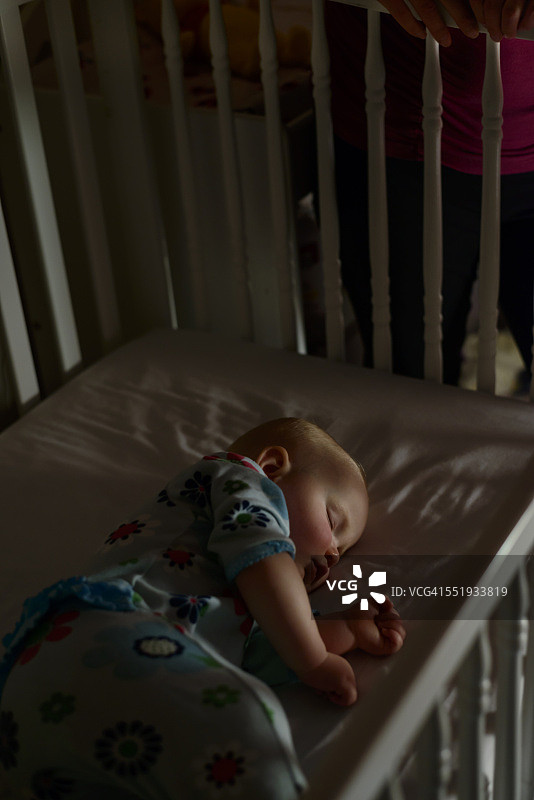 宝宝晚上在婴儿床里睡觉，妈妈在婴儿床旁图片素材