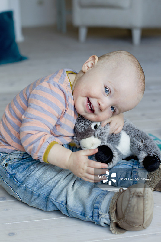 坐在客厅地板上拥抱毛绒玩具的女婴肖像图片素材