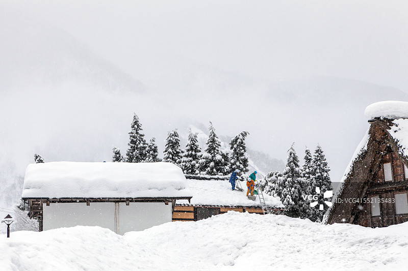 在冬季暴风雪中，男人们正在清除屋顶上的积雪图片素材