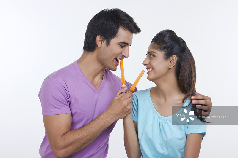 快乐的年轻夫妇在白色背景下互相喂橙色冰棒图片素材