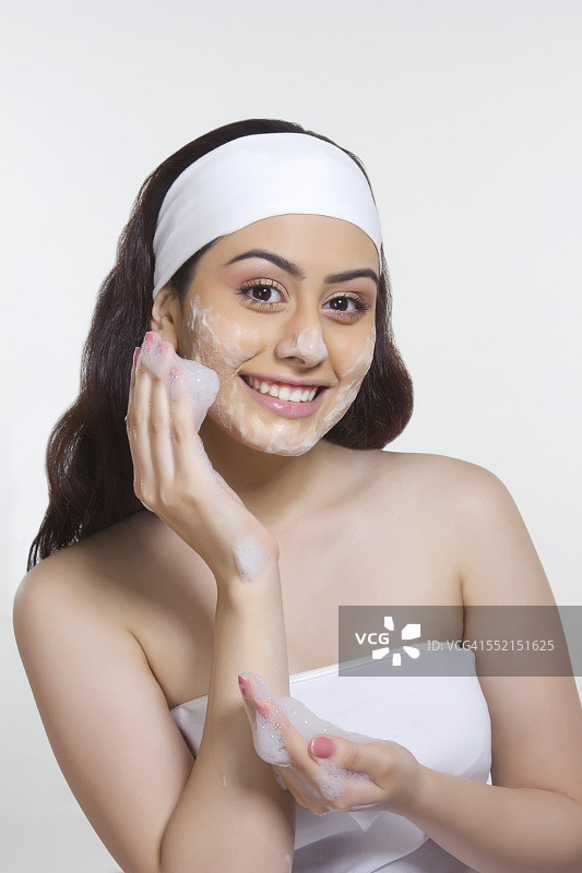 在白色背景下往脸上涂抹肥皂的微笑女人肖像图片素材