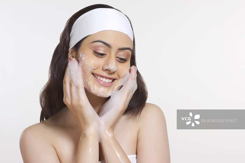 微笑的女人在白色背景下在脸上涂抹肥皂图片素材