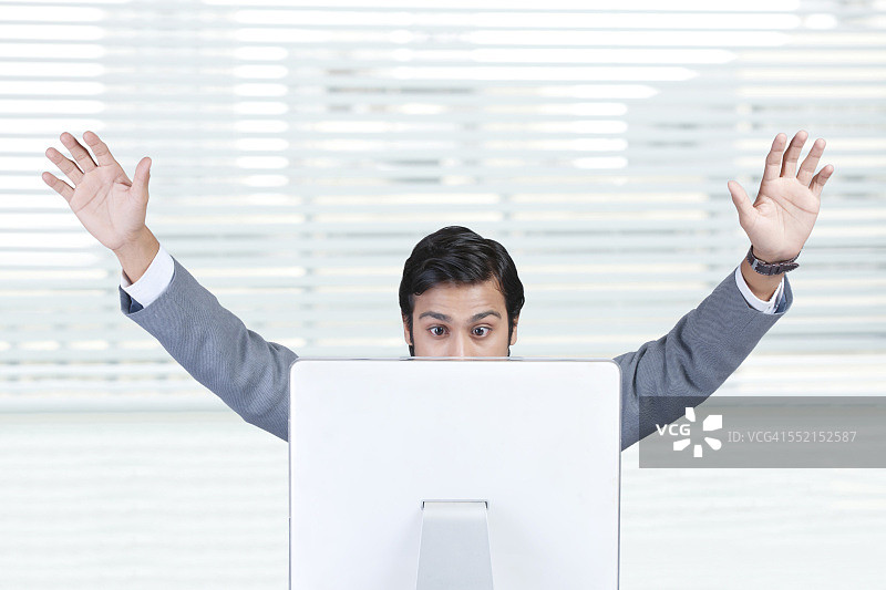 震惊的商人举起双臂看着办公室里的笔记本电脑图片素材