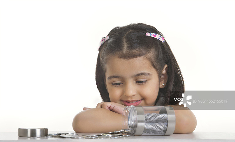 女孩看着洒在白色背景桌子上的印度硬币图片素材