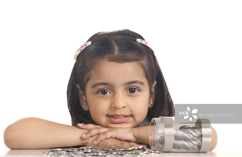 白色背景下，桌子上洒满印度硬币的可爱女孩肖像图片素材