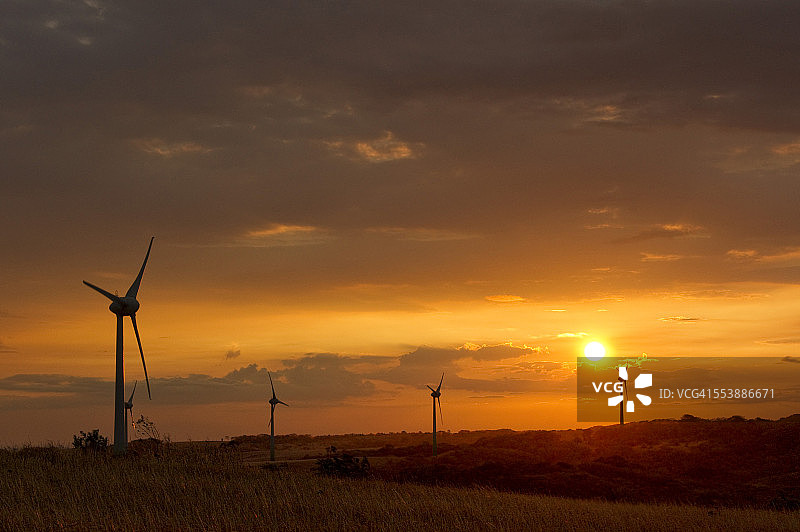 日落时丘陵景观中的风车涡轮机图片素材