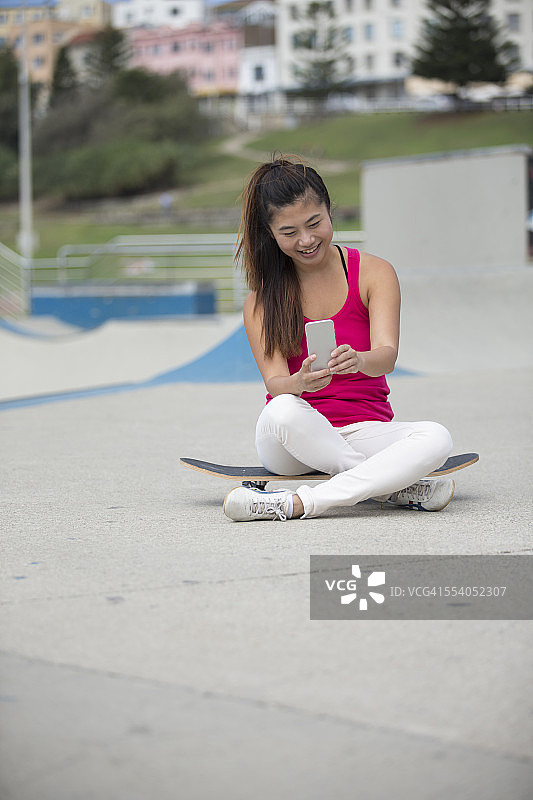 中国女人在滑板公园使用智能手机图片素材