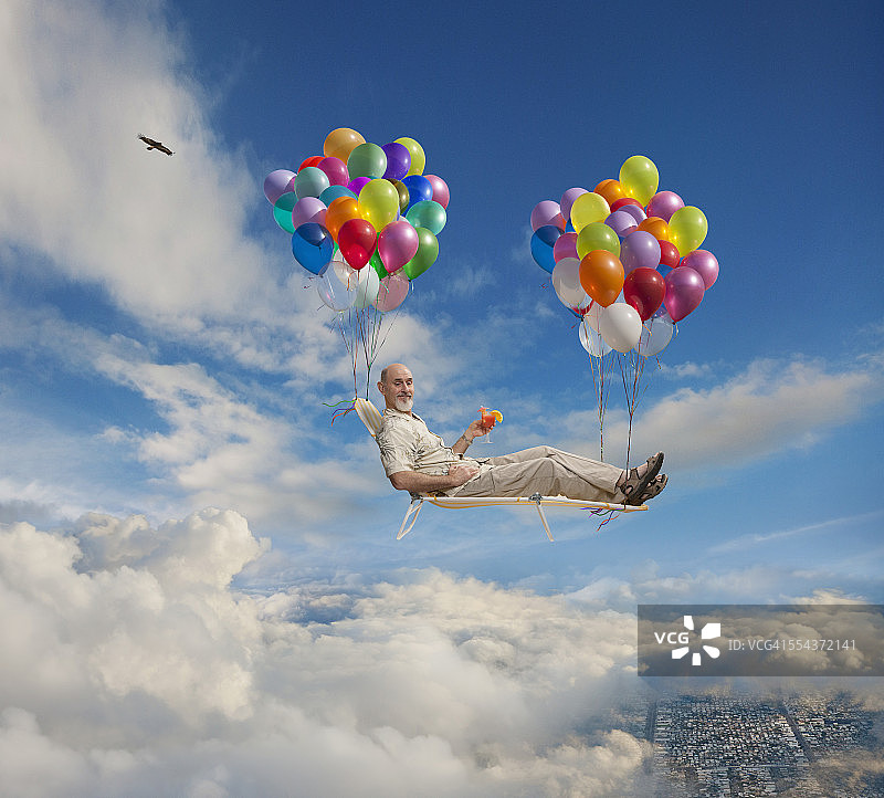 白人男子坐在草坪椅上，与气球一起漂浮在空中图片素材