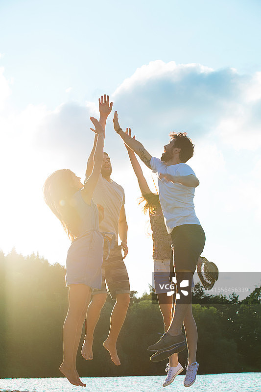 在逆光下的湖边击掌的四个朋友图片素材