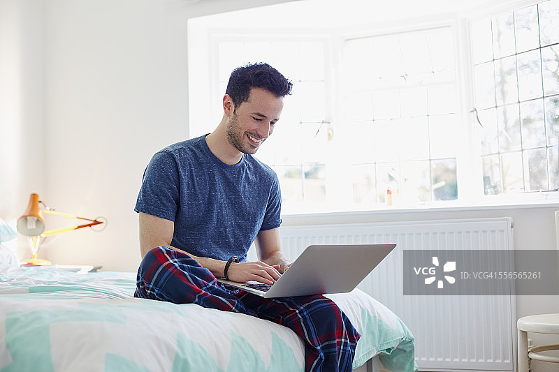 在卧室里使用笔记本电脑的年轻男人图片素材